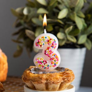 Lit number 3 sprinkles candle featuring bright candy-like dots, styled as a cheerful cake topper for kids birthday parties.
