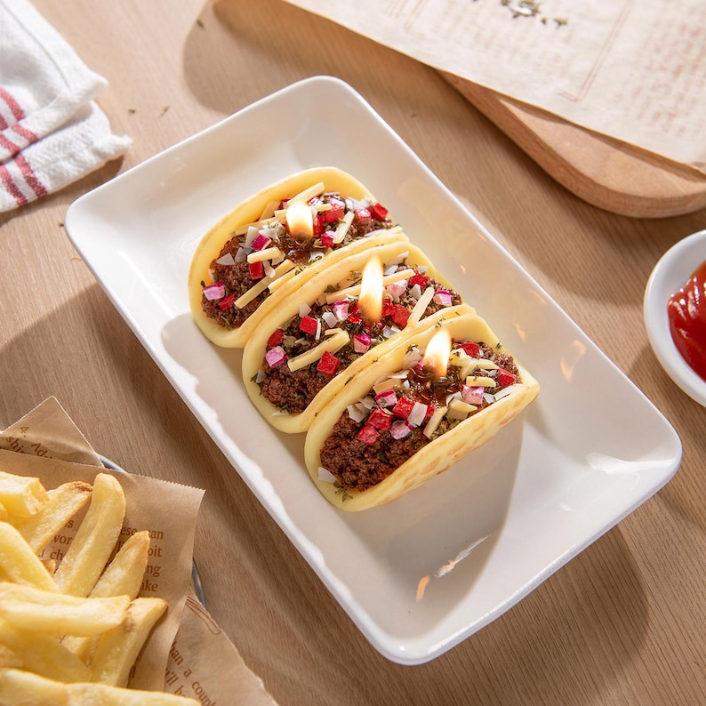Bird’s-eye view of realistic taco candle lit with glowing wick, featuring wax taco shell filled with ground beef, onions, and sprinkled cheese wax melts. Handmade novelty candle, perfect Mexican gift and unique taco lover gift