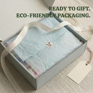 May include: A light blue gift box with a white ribbon and a blank tag. Inside, the box contains tissue paper and a small sticker that says "thank you". The text "READY TO GIFT. ECO-FRIENDLY PACKAGING." is printed above the box.