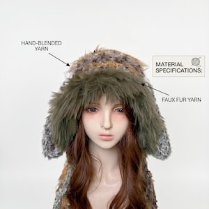 May include: A faux fur hat with ear flaps. The hat is made with hand-blended yarn and faux fur yarn. The hat has a mix of brown, gray, and green colors. The text on the image reads "MATERIAL SPECIFICATIONS:" and "HAND-BLENDED YARN" and "FAUX FUR YARN".
