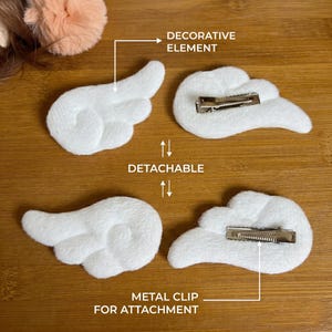 May include: White plush angel wing hair clips with metal clips for attachment. The decorative elements are detachable. The image shows two pairs of white plush angel wing hair clips, each with a metal clip on the back for easy attachment to hair.