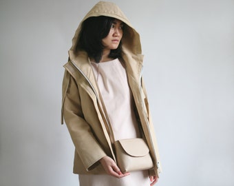 May include: A beige hooded jacket with a zipper closure and a small beige crossbody bag. The jacket has a relaxed fit and a casual style.
