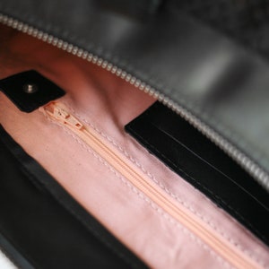 May include: The inside of a black handbag with a pink lining and a zipper closure. The zipper is open and the lining is visible.