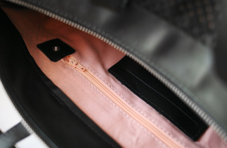 May include: The inside of a black handbag with a pink lining and a zipper closure. The zipper is open and the lining is visible.