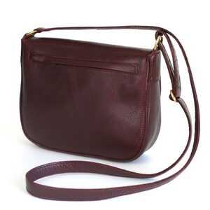 Pu&ograve; includere: Una borsa a tracolla in pelle bordeaux con un lungo cinturino regolabile. La borsa ha una chiusura a lembo e una piccola tasca sul retro.