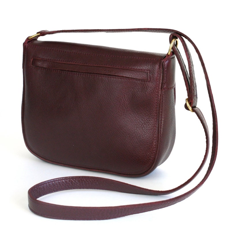 Pu&ograve; includere: Una borsa a tracolla in pelle bordeaux con un lungo cinturino regolabile. La borsa ha una chiusura a lembo e una piccola tasca sul retro.