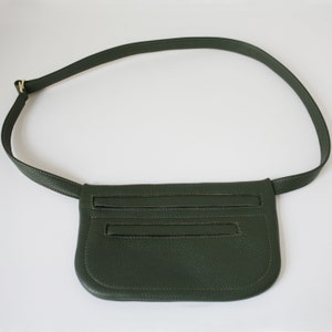 Pode incluir: Uma pochete de couro verde escuro com uma al&ccedil;a longa ajust&aacute;vel. A bolsa tem dois compartimentos com z&iacute;per e um fecho de aba.