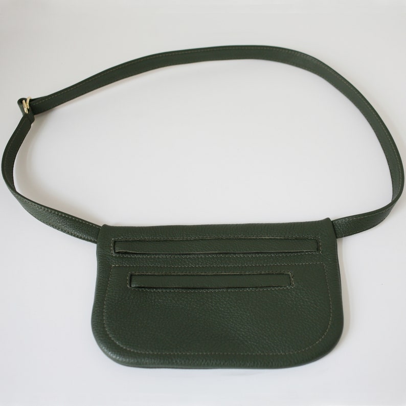 Pode incluir: Uma pochete de couro verde escuro com uma al&ccedil;a longa ajust&aacute;vel. A bolsa tem dois compartimentos com z&iacute;per e um fecho de aba.