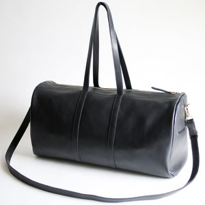 May include: A black leather duffel bag with a long shoulder strap and two top handles. The bag has a gold zipper and a gold clasp.