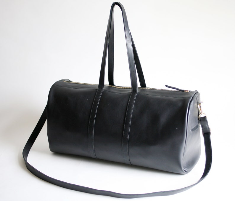 May include: A black leather duffel bag with a long shoulder strap and two top handles. The bag has a gold zipper and a gold clasp.