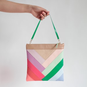 Puede incluir: Bolso de mano colorido con un patrón geométrico de chevron en rosa, rojo, morado, verde y azul. La parte superior es de color beige claro, con una correa verde y detalles dorados.
