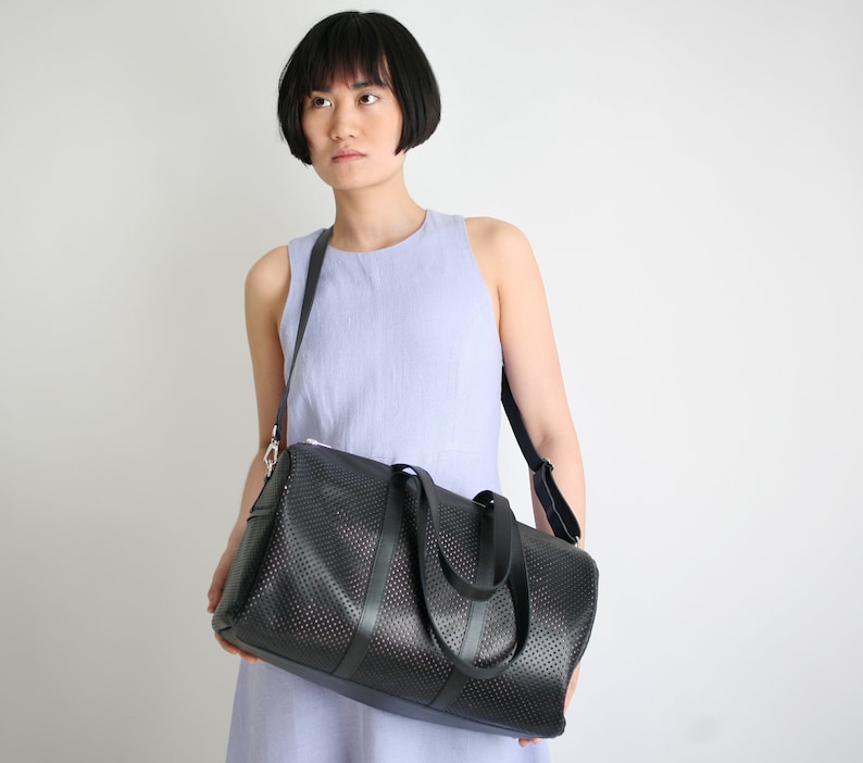 May include: A black leather duffel bag with a perforated design. The bag has a long strap and two shorter handles.