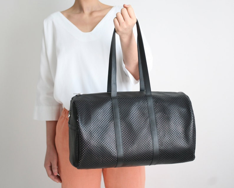 May include: A black leather duffel bag with a perforated design and black straps. The bag has a zipper closure.