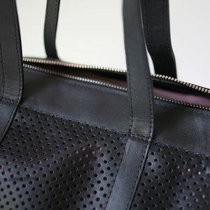 May include: Black leather tote bag with a perforated design and a zipper closure. The bag has two top handles.