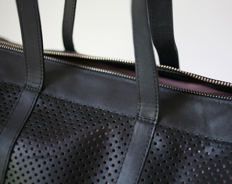 May include: Black leather tote bag with a perforated design and a zipper closure. The bag has two top handles.