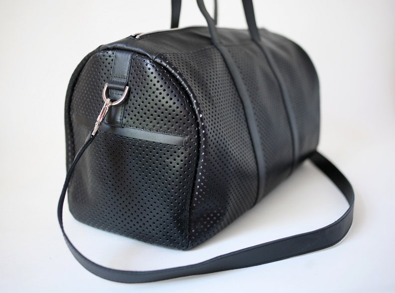 May include: A black leather duffel bag with a perforated design and a long adjustable strap. The bag has a silver metal hook on the side.