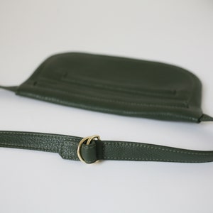 Pode incluir: Uma bolsa de ombro de couro verde escuro com uma fivela de metal dourado. A bolsa tem um fecho de aba e uma al&ccedil;a longa ajust&aacute;vel.