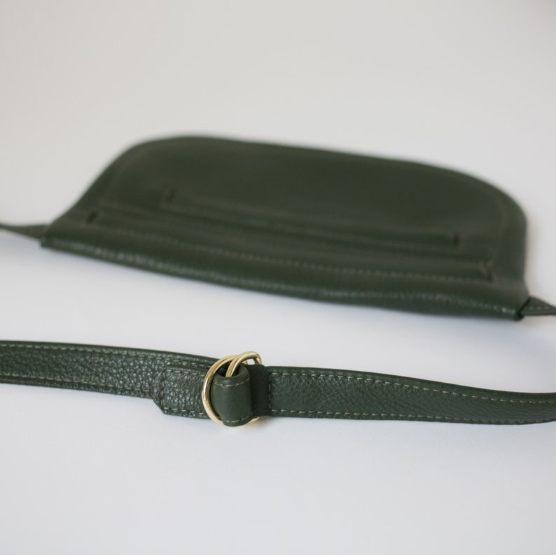 Pode incluir: Uma bolsa de ombro de couro verde escuro com uma fivela de metal dourado. A bolsa tem um fecho de aba e uma al&ccedil;a longa ajust&aacute;vel.