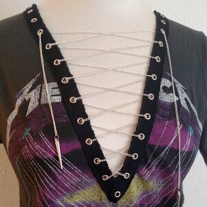 May include: A black t-shirt with a graphic print and a silver chain detail across the neckline. The chain is laced through grommets on the shirt.