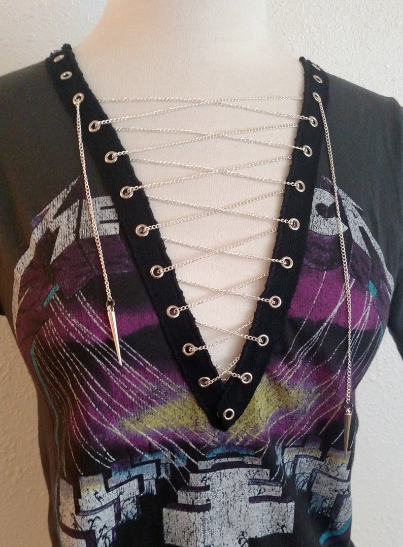 May include: A black t-shirt with a graphic print and a silver chain detail across the neckline. The chain is laced through grommets on the shirt.