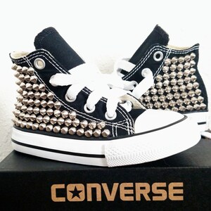 May include: Black high-top Converse sneakers with silver studs covering the sides. The shoes are in a box with the Converse logo.
