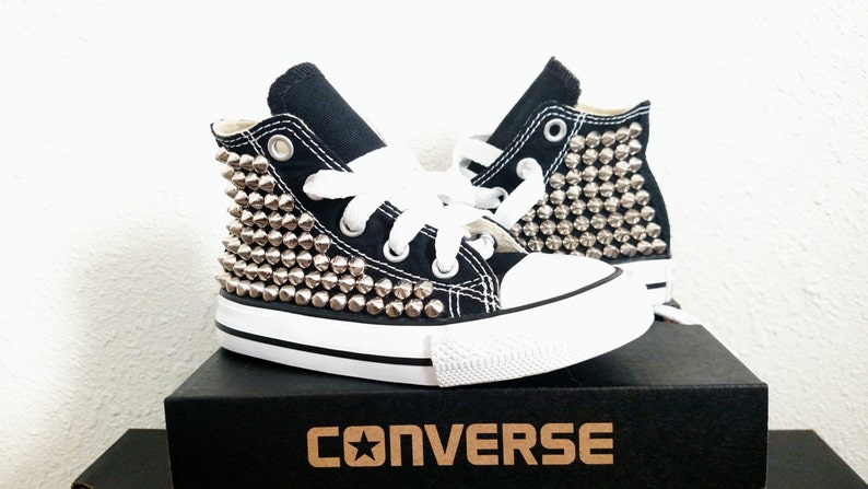 May include: Black high-top Converse sneakers with silver studs covering the sides. The shoes are in a box with the Converse logo.