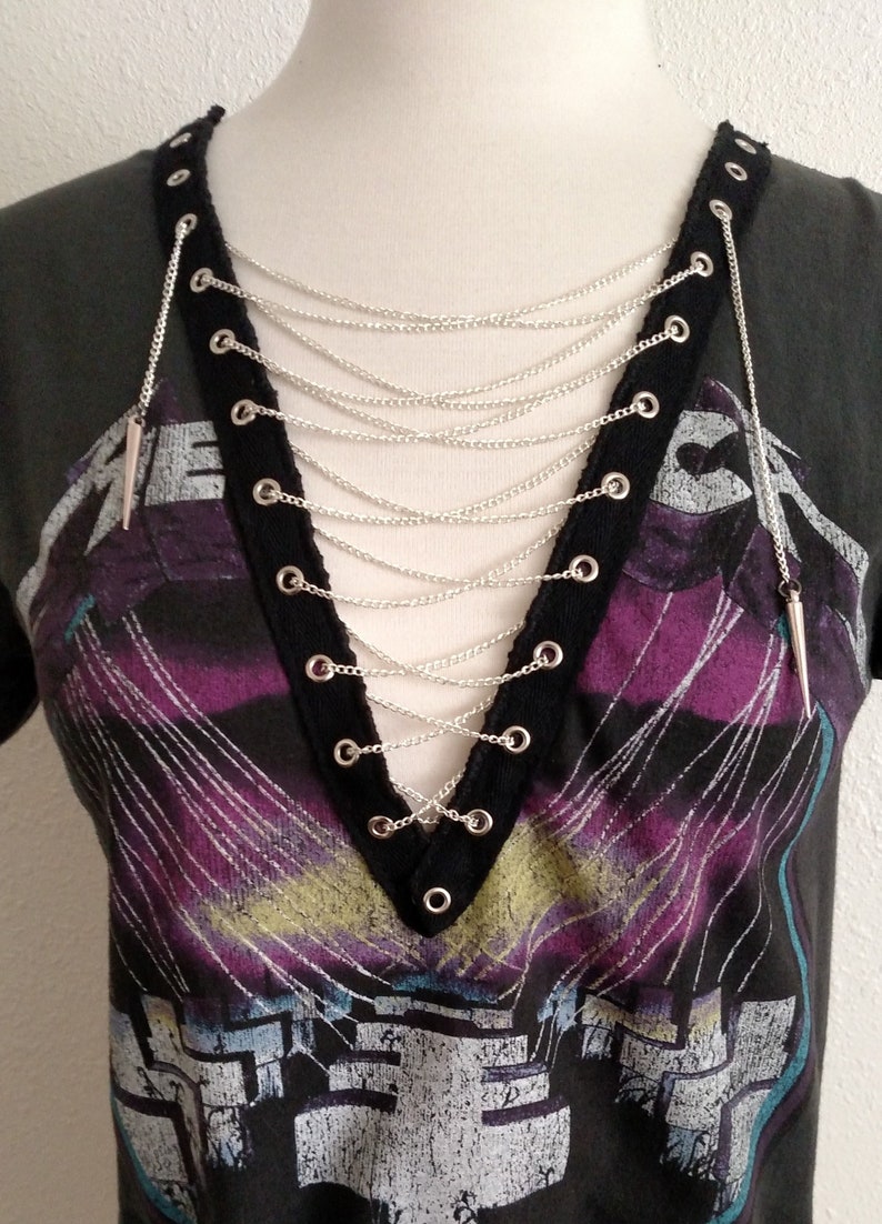 May include: A black t-shirt with a graphic print and a silver chain necklace with spikes. The chain is laced through grommets on the shirt.
