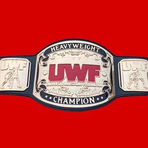 以下が含まれることがあります： 「HEAVYWEIGHT」と「UWF CHAMPION」の文字が入った、金と黒のレスリングチャンピオンベルト。中央のプレートには赤い文字で「UWF」と書かれています。サイドプレートにはレスリングの姿が描かれています。