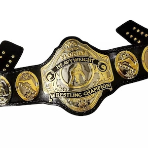 May include: A black leather wrestling championship belt with gold and silver accents. The belt features the text "NWA FLORIDA HEAVYWEIGHT WRESTLING CHAMPION" and a central emblem of a wrestler. Additional gold medallions are on the belt.