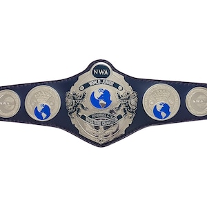 May include: A blue and silver NWA World Junior Championship belt. The belt features a large central emblem with a globe design, flanked by lion figures. The text "WORLD JUNIOR" and "HENNWELGTE WESSTUNG CHANTRON" are visible.