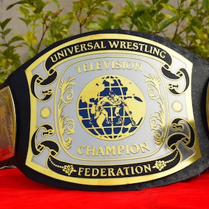 May include: A wrestling championship belt with a black leather strap and gold and silver accents. The center plate features a globe with two wrestlers and the text "UNIVERSAL WRESTLING TELEVISION CHAMPION FEDERATION".