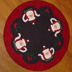 May include: Round, red and black felt Christmas table topper with four Santa teapot designs. The teapot designs have white trim and a red Santa hat.