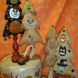 May include: A collection of handmade Halloween tree decorations. The trees feature whimsical faces, including a witch, a snowman, and a pumpkin. The trees are made of fabric and adorned with buttons and other embellishments. The color palette includes black, orange, and beige.