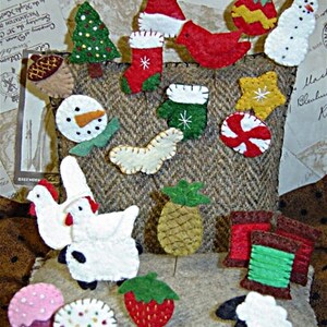 Puede incluir: Una colección de adornos de fieltro en varias formas y colores. Incluye un árbol de Navidad, un muñeco de nieve, un gorro de Papá Noel y otros diseños festivos. Los adornos están dispuestos sobre un fondo de tela marrón texturizada.