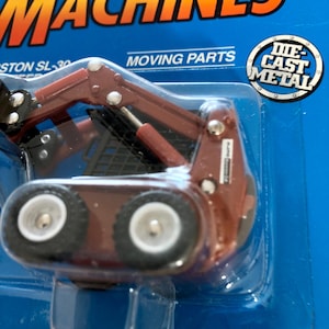 May include: A red toy farm machine with moving parts. The toy is made of die-cast metal and has a black plastic cab. The toy is packaged on a blue background with the words "Farm Machines" and "Moving Parts" printed on it.