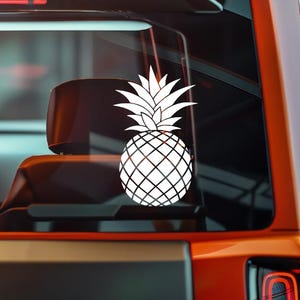 Op de afbeelding: Een witte ananassticker met een gedetailleerd rasterpatroon en stekelige kroon is aangebracht op een autoraam. Het ontwerp is een tropische vrucht, geschikt voor autodecoratie.