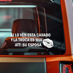 May include: A white vinyl decal with text in Spanish, reading "SI LO VEN ESTA CASADO Y LA TROCA ES MIA ATT: SU ESPOSA" and a graphic of lips. The decal is applied to a vehicle's rear window.
