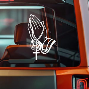 May include: White decal of praying hands with a rosary and a cross. The hands are clasped together in a gesture of prayer. The rosary beads are draped between the hands, and a cross hangs from the rosary.