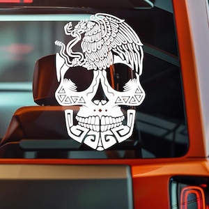 Puede incluir: Calcomanía blanca de una calavera estilizada con un diseño de águila y serpiente, un símbolo de México. La calcomanía está aplicada a la ventana de un vehículo, mostrando los intrincados detalles de la obra de arte. El diseño es audaz.