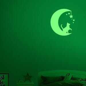 Könnte beinhalten: Ein leuchtend grüner Wandaufkleber mit einem Halbmond, einer Katzen-Silhouette und Sternen. Die Katze sitzt auf dem Mond und bildet ein skurriles, himmlisches Design. Der Aufkleber leuchtet im Dunkeln und ist ideal für Kinderzimmer.