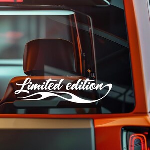 以下が含まれることがあります： 車両の後部窓に貼られた、波模様のデザインが施された白い「限定版」ステッカー。車両はオレンジ色のボディと黒色の内装で、光沢のある仕上がりです。