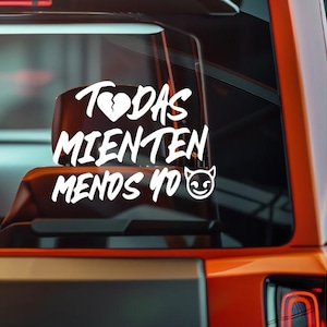 Op de afbeelding: Witte vinyl sticker met de Spaanse tekst "TODAS MIENTEN MENOS YO" en een gebroken hart symbool. De sticker heeft ook een lachend duivelsgezicht. De sticker is aangebracht op de achterruit van een oranje voertuig.