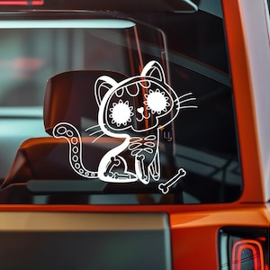 May include: A white vinyl decal of a cat in the style of a Day of the Dead sugar skull. The cat has a skeleton body and a bone. The decal is on a car window.
