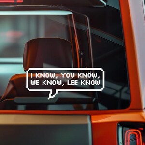 May include: A white sticker with black text in a speech bubble that reads "I KNOW, YOU KNOW, WE KNOW, LEE KNOW" is adhered to a car window. The sticker is in front of a car seat and part of the car's exterior.