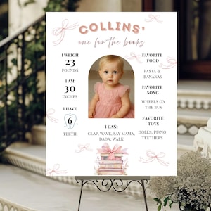 May include: A white milestone birthday sign featuring the name Collins, pink ribbon illustrations, and a central photo of a child in a pink dress. Text includes weight of 23 pounds, height of 30 inches, 6 teeth, favorite foods, songs, and toys.