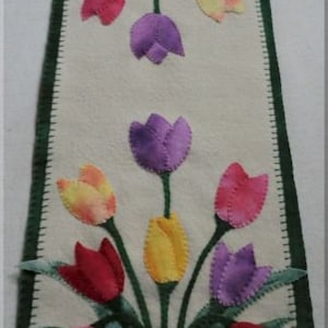 May include: A rectangular, off-white felt wall hanging with a green scalloped border. The design features colorful felt tulips in shades of red, pink, yellow, and purple. The text "©2018 Cath's Pennies Designs" is at the bottom.