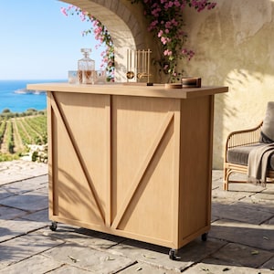 May include: A rectangular light wood bar cart featuring a front panel with two diagonal support beams and four black caster wheels. The top surface holds a glass decanter, two matching glasses, a gold-toned bar tool set, and coasters.