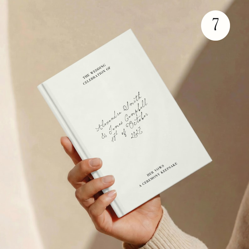 May include: A white hardback book featuring black printed text which reads THE WEDDING CELEBRATION OF, Alexandra Smith & James Campbell 18th of October 2027, and HER VOWS A CEREMONY KEEPSAKE. The cover displays a simple, clean design with elegant lettering.