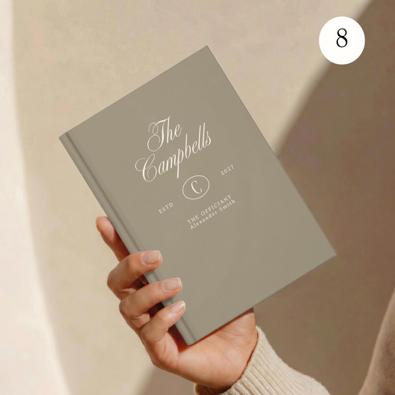 May include: A rectangular, taupe-colored notebook featuring white printed text that reads The Campbells, ESTD, 2027, a circular emblem with the letter C, and the text THE OFFICIANT Alexander Smith. The cover has a smooth, matte finish.
