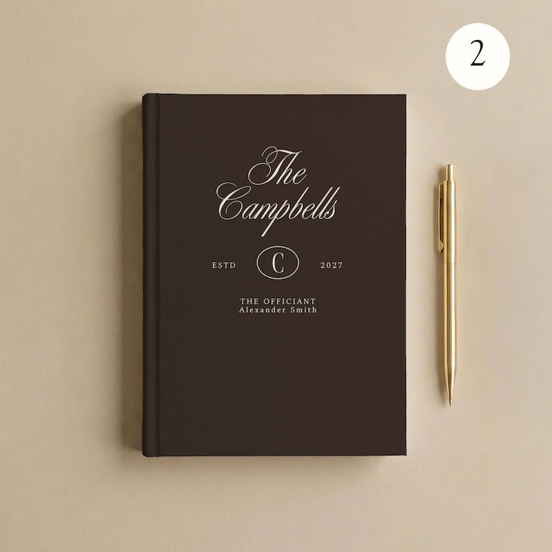 May include: A dark brown hardcover book with white text reading The Campbells, ESTD 2027, and THE OFFICIANT Alexander Smith, featuring a central oval with the letter C. A gold-colored metal pen is positioned vertically to the right of the book.